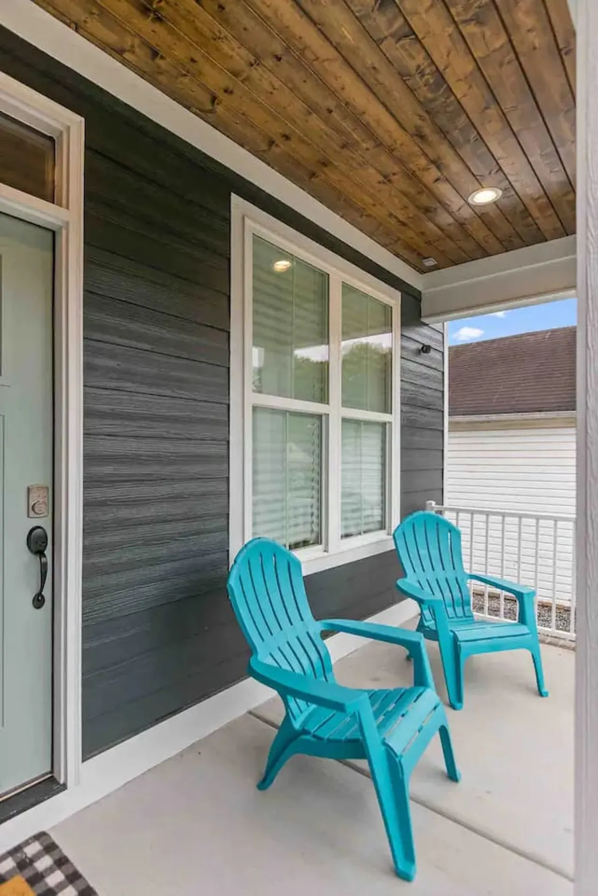 The photo captures the home's inviting exterior with turquoise chairs arranged on a covered porch near the front door. The setting is accented by a warm wooden ceiling, suggesting a welcoming space to gather before or after an evening out. The ambient light hints at sunset, evoking the energy and relaxation that comes with returning from a night downtown.
