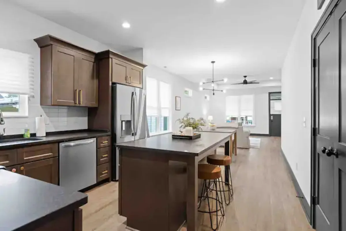 A well-lit kitchen scene featuring a large island, stainless steel appliances, and wooden cabinetry. The design balances warmth and functionality, inviting guests to cook, entertain, and gather comfortably.