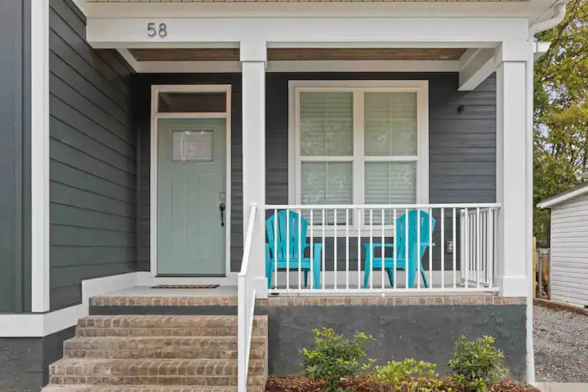 The image shows the front door area with blue chairs, steps, and the house number, all bathed in gentle, natural light. The inviting porch setting enhances the sense of safety and tranquility, providing a view that immediately sets a comforting tone for anyone approaching or leaving the house.