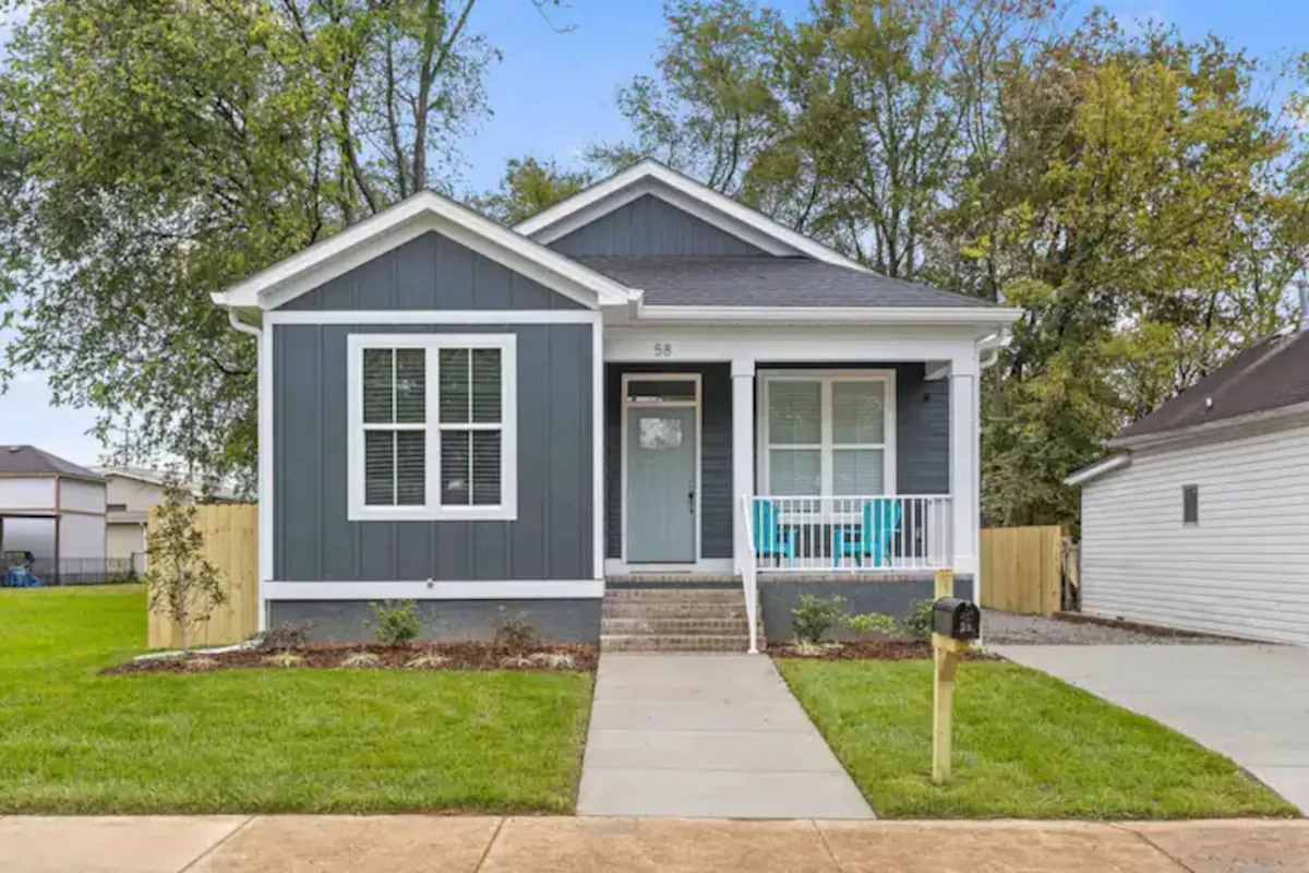 A view of the property’s front porch featuring turquoise chairs, a well-manicured lawn, and distinctive gray siding. The inviting entry suggests a welcoming home base after exploring the city, while the outdoor seating hints at moments of relaxation and connection to the neighborhood.