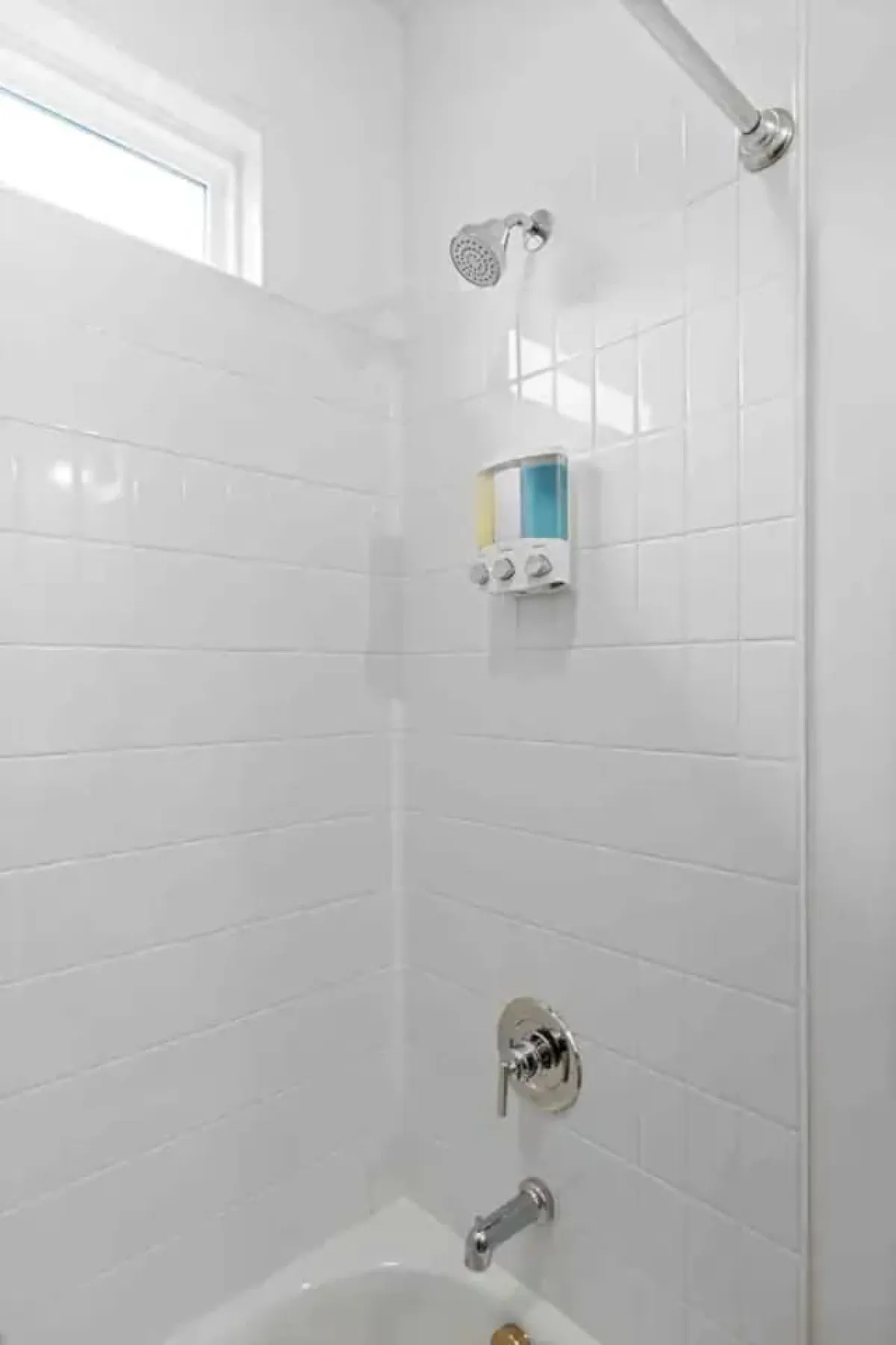 A modern bathroom featuring a prominent showerhead, soap dispenser, and sleek tiled walls. The clean design and fresh atmosphere suggest both convenience and relaxation.