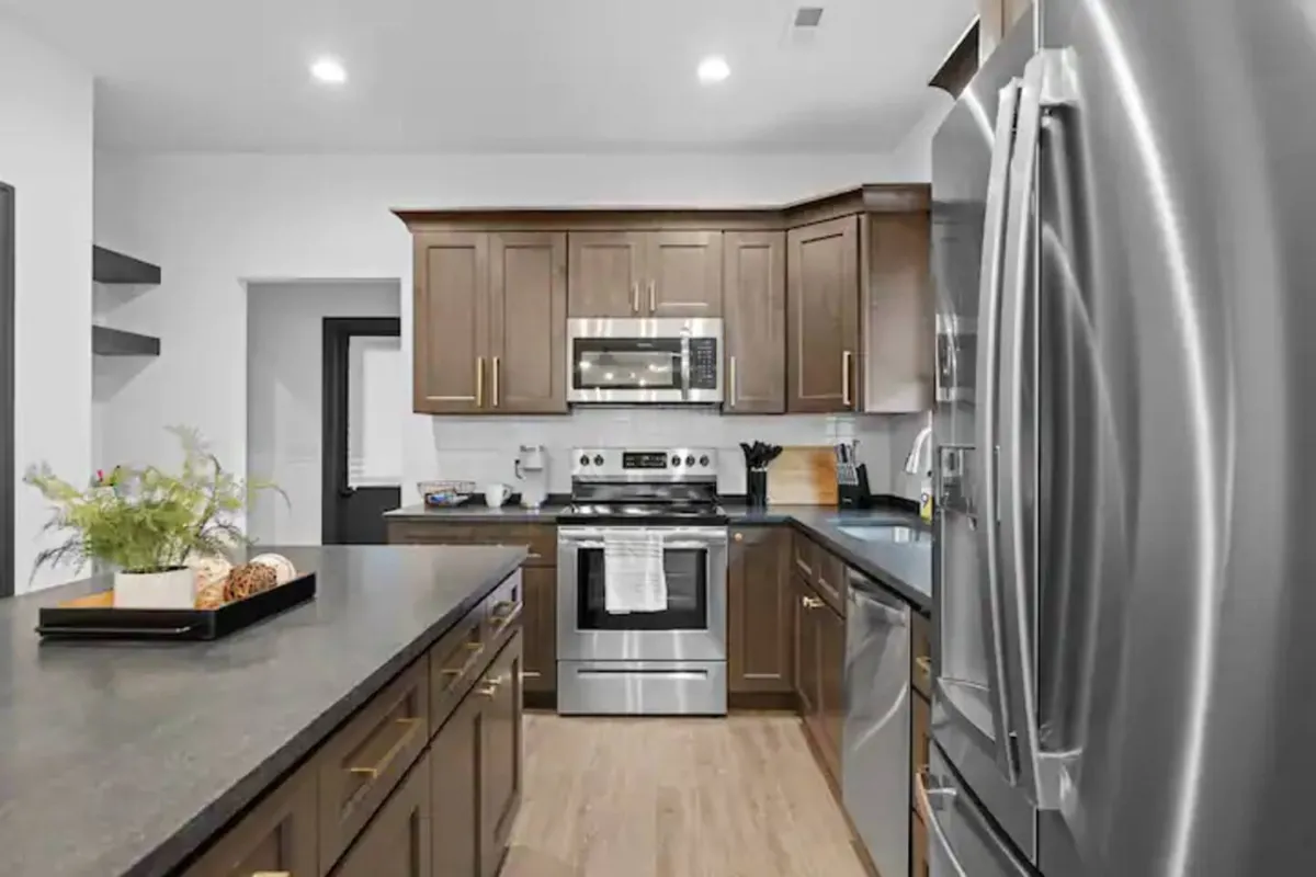 A bright, modern kitchen with a central island, stainless steel appliances, and warm wooden cabinetry is pictured. The space is functional, inviting, and highlights the home’s new build quality.