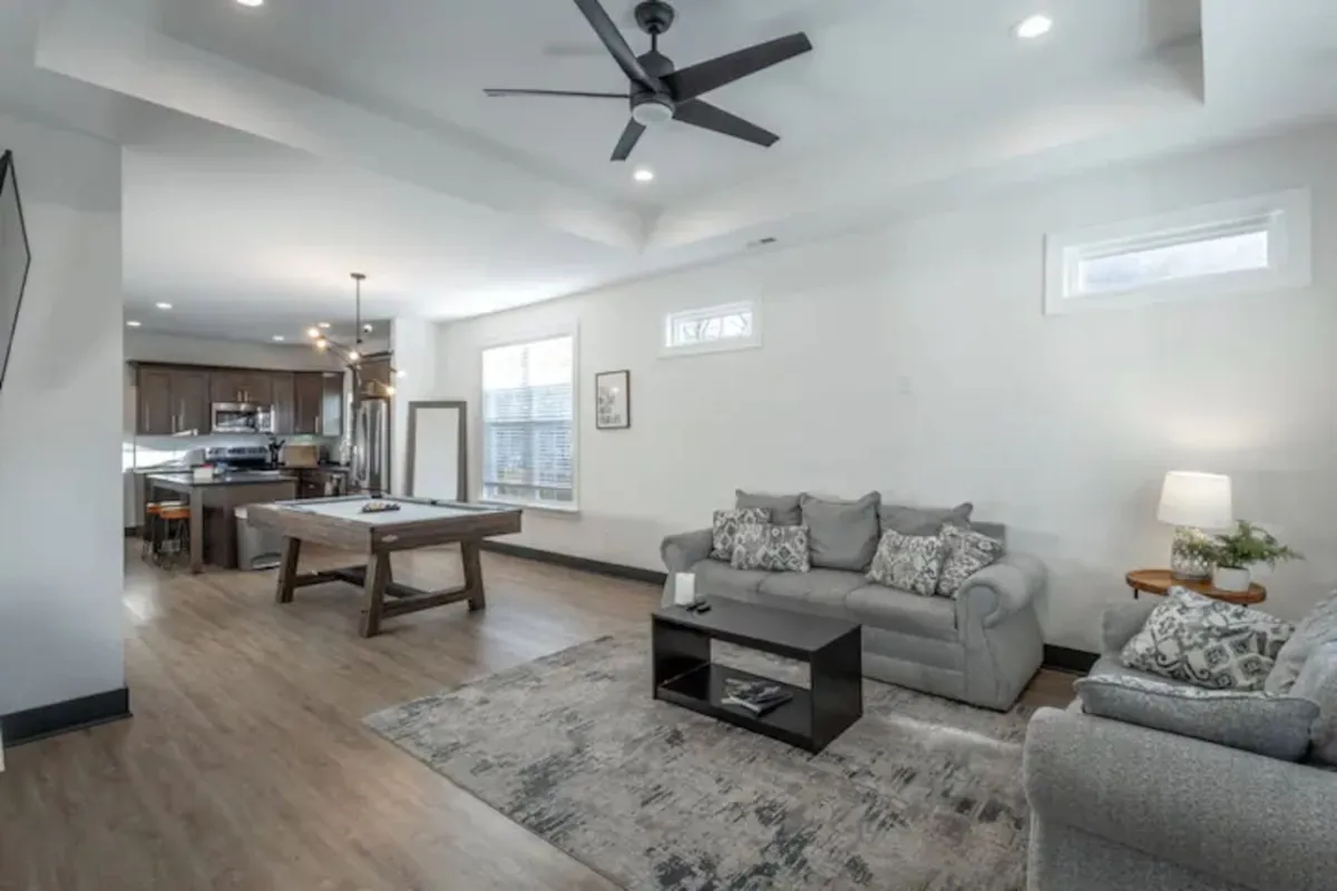 The photograph shows a comfortable living space with a sofa adorned with decorative cushions, a wooden coffee table, and the kitchen area in the background. The open layout is ideal for family gatherings and socializing, and it reflects the property's newly built, modern feel.